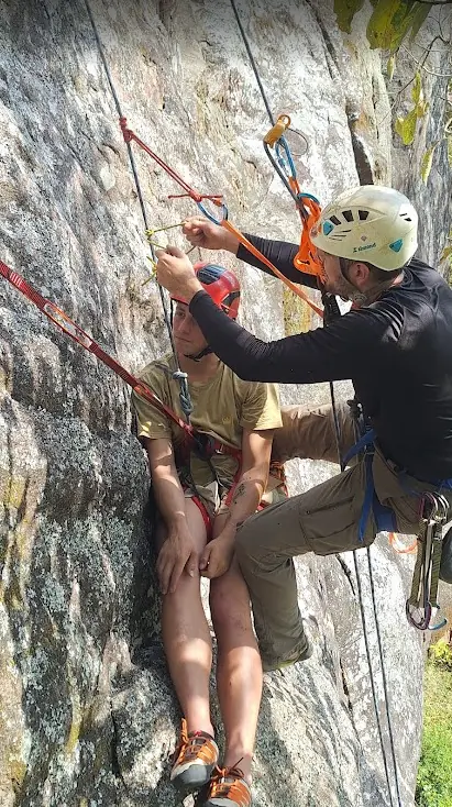 Instrutor ajustando o sistema de cordas de um aluno sentado na cadeirinha, suspenso na rocha