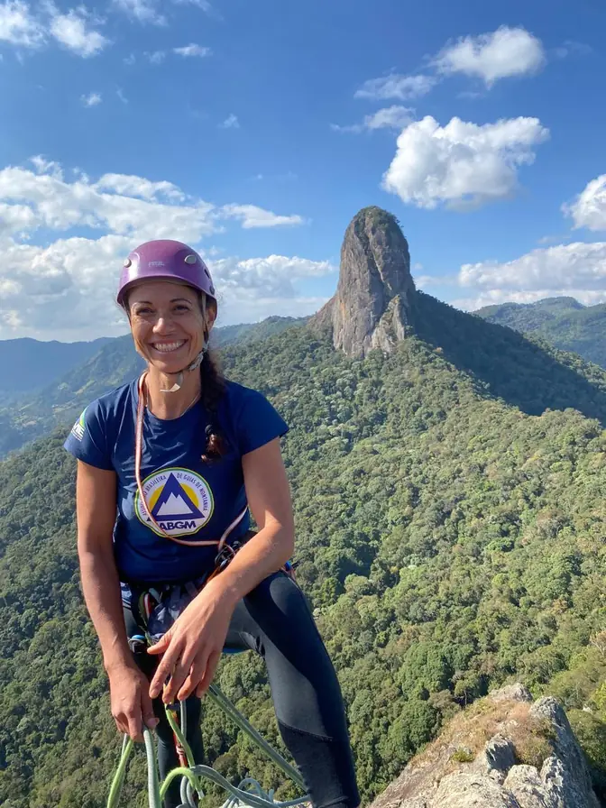 Retrato de Danielle Pinto sorrindo, de capacete, com a Pedra do Baú ao fundo