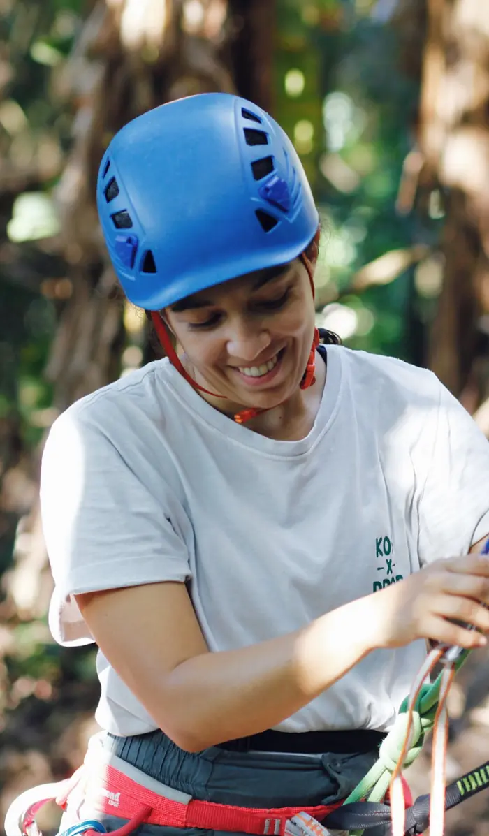 Aluna sorrindo enquanto confere um nó na corda presa ao equipamento
