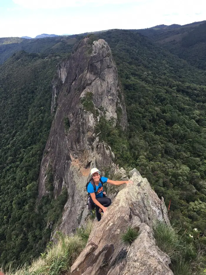 Escaladora na aresta de uma agulha de granito cercada de mata na Serra da Mantiqueira