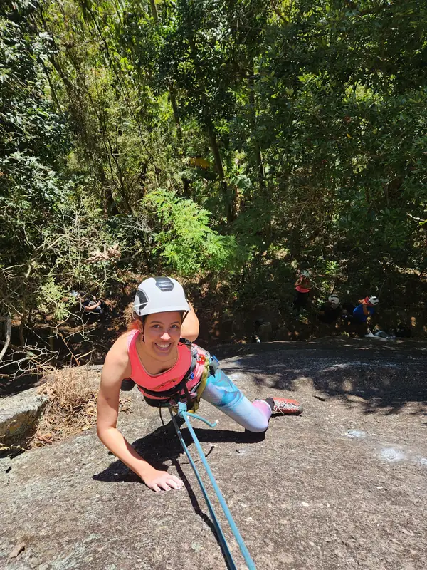 Escaladora subindo laje de rocha em aderência cercada de mata