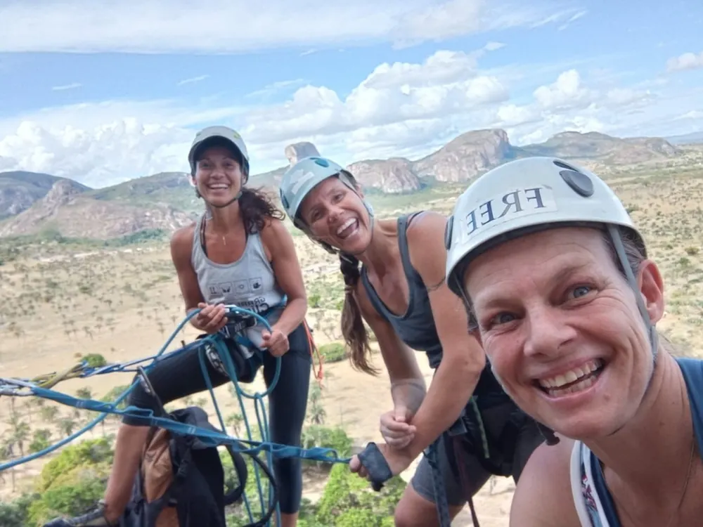 Grupo de escaladoras sorrindo em um platô de rocha com paisagem de montanhas ao fundo