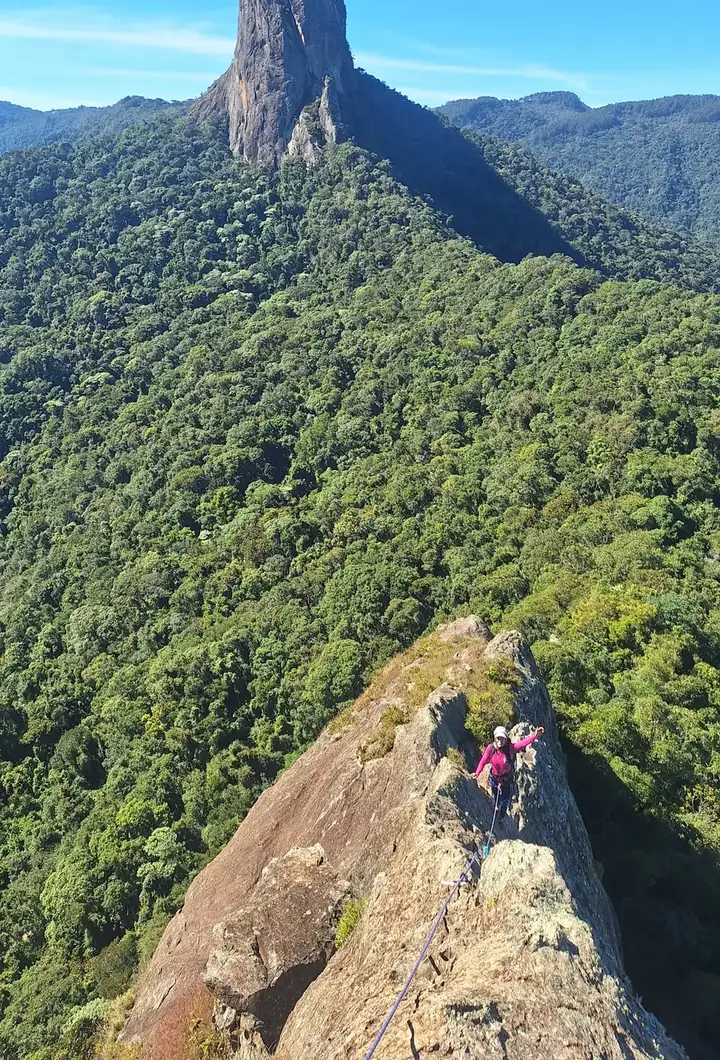 Escaladora na crista de rocha da Ana Chata, com o Bauzinho e a mata da Mantiqueira à frente