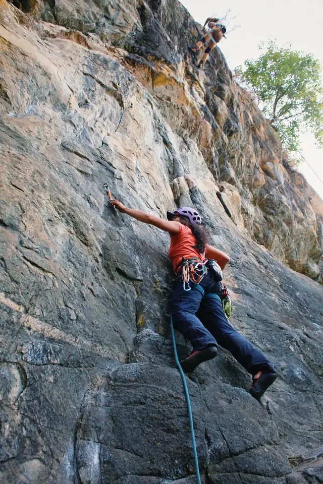 Escaladora de capacete lilás clipando a costura na parede de rocha