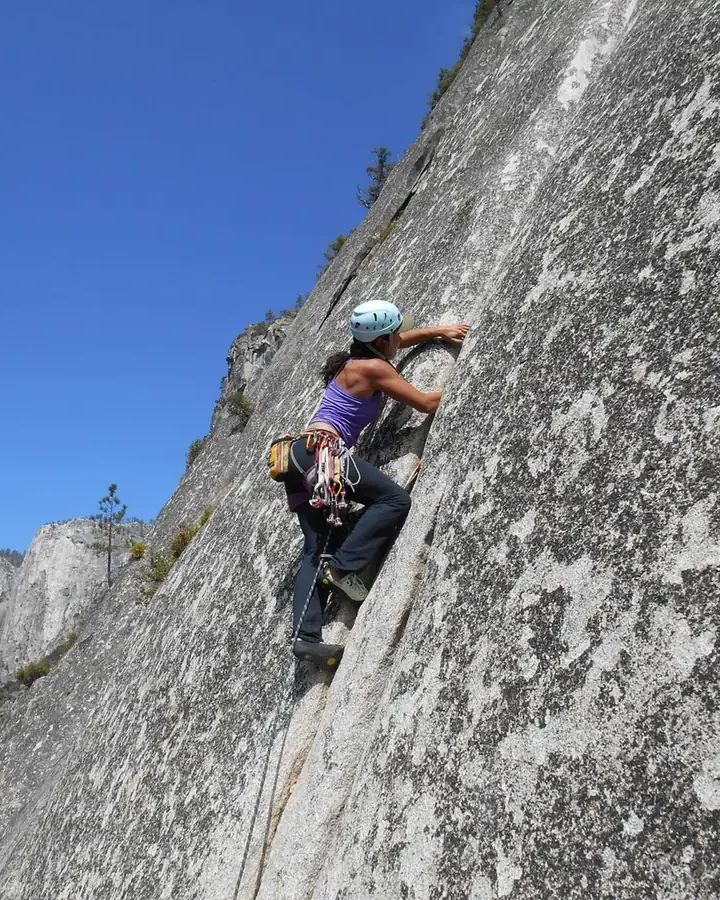 Danielle Pinto escalando uma grande parede de granito, com o vale ao fundo
