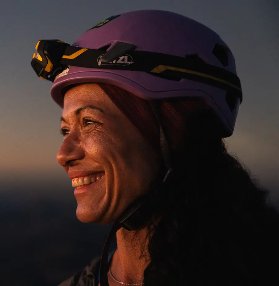 Danielle Pinto sorrindo ao entardecer, de capacete lilás e lanterna de cabeça