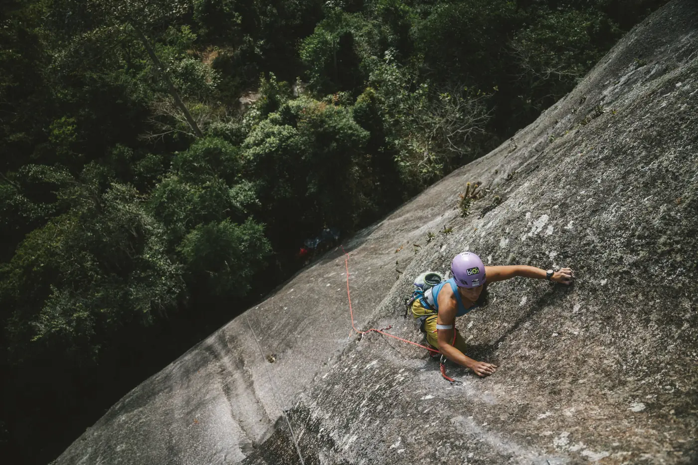 Vista de cima: Danielle Pinto escalando uma grande placa de granito, com a mata lá embaixo