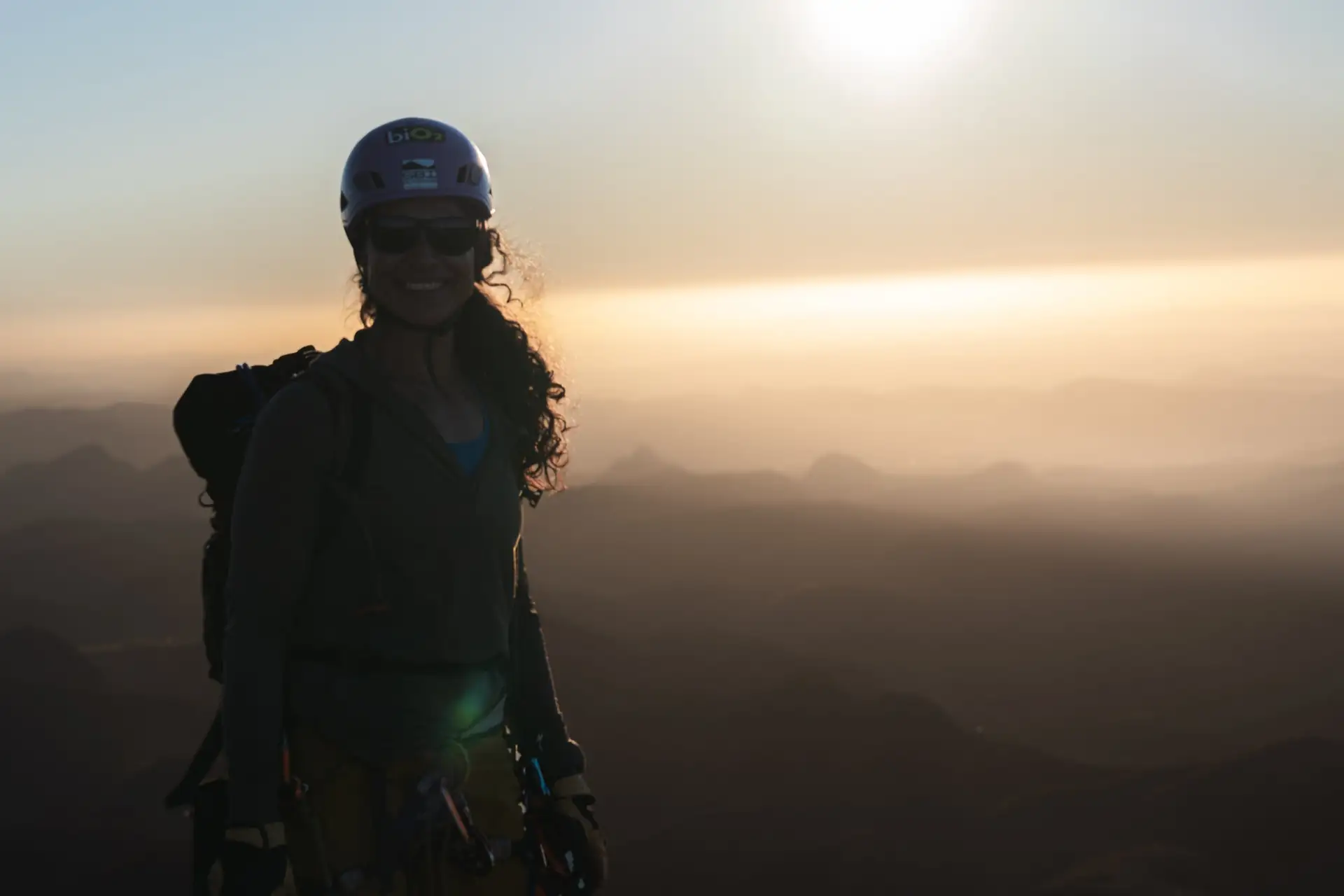 Silhueta de Danielle Pinto com o cabelo ao vento ao pôr do sol, no alto da montanha