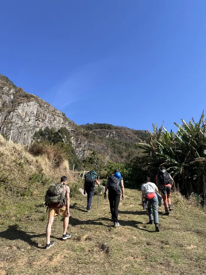 Grupo caminhando pela trilha até a rocha, com céu azul e montanhas